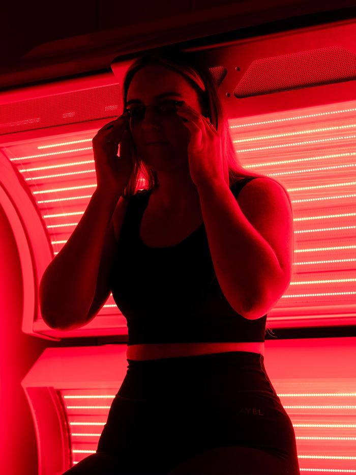 Woman putting on protective eyewear before a full-body red light therapy session at The Tanning Shop UK