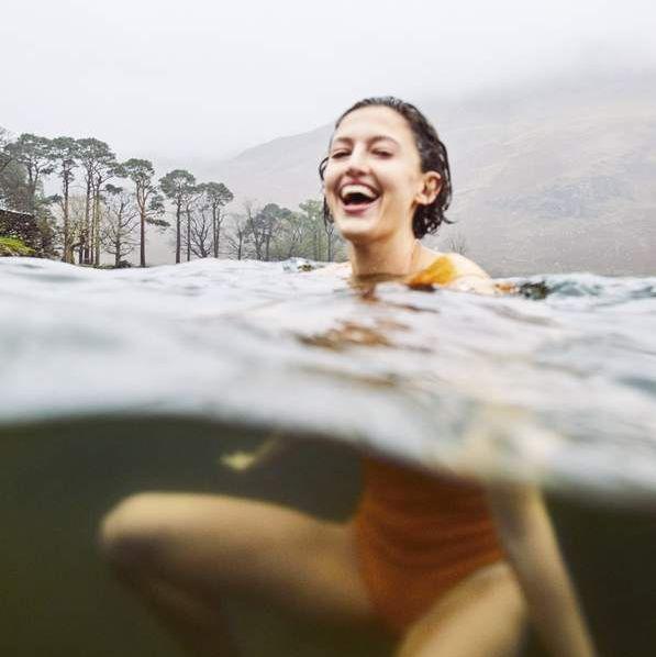Wild swimming cold water immersion therapy - woman laughing while swimming in cold open water lake