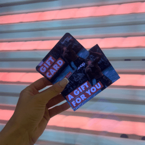 Hand holding The Tanning Shop gift card in front of UV tanning bed lamps