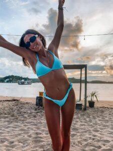 Woman with glowing tanned skin in blue bikini posing on beach for The Tanning Shop UK blog