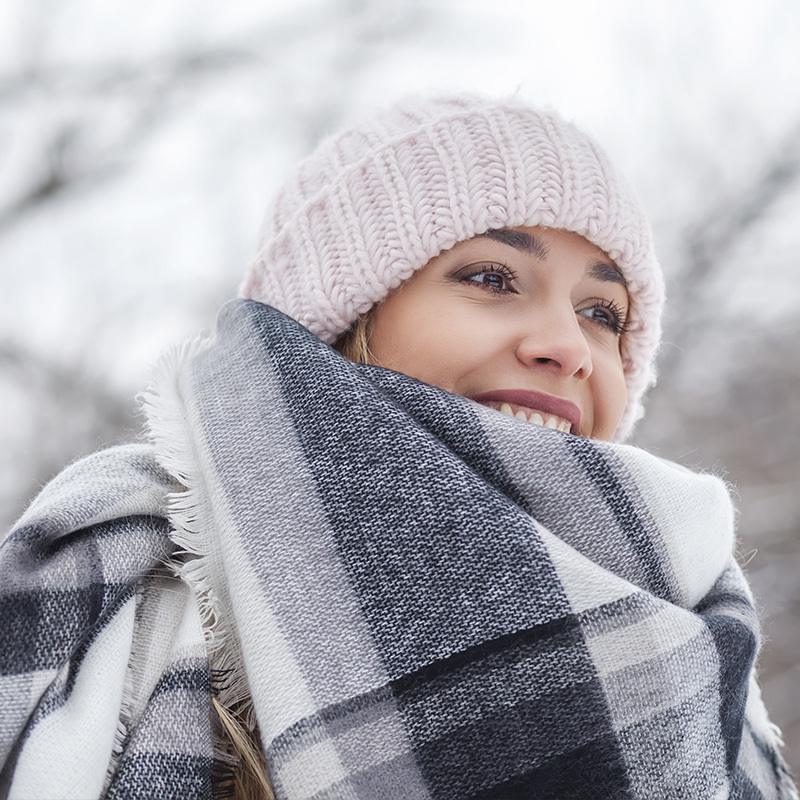 Happy woman in winter hat and scarf smiling outdoors for winter tanning blog