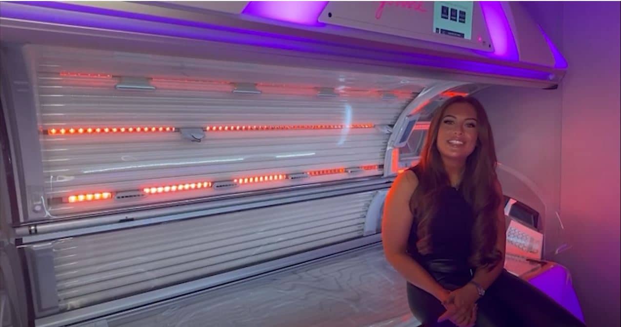 Woman standing next to premium tanning bed with orange LED lighting for beginners guide to tanning at The Tanning Shop UK
