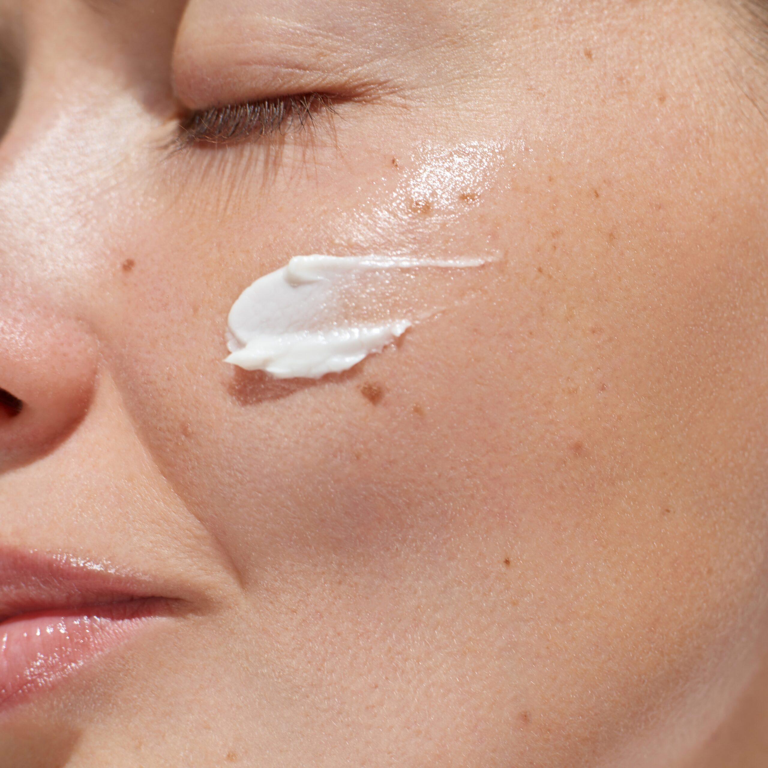 Close up of woman applying tanning cream moisturiser to face for glowing skin