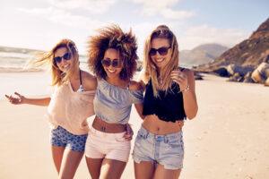 Three diverse tanned women friends laughing on the beach - achieve a glowing tan at The Tanning Shop UK