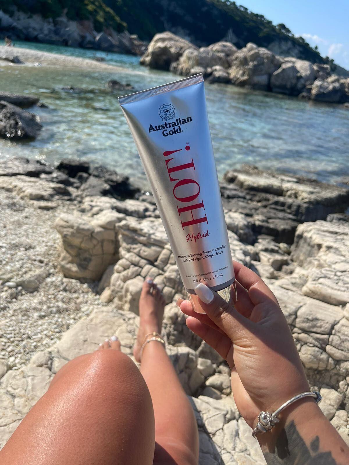 Sunbed tips for beginners - woman holding Australian Gold HOT! tanning lotion at beach The Tanning Shop UK