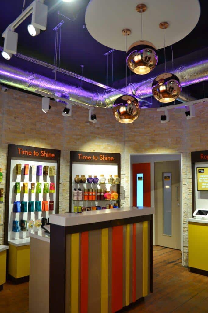 The Tanning Shop salon interior showing reception counter with striped panels, product display shelves, copper pendant lights and Time to Shine signage