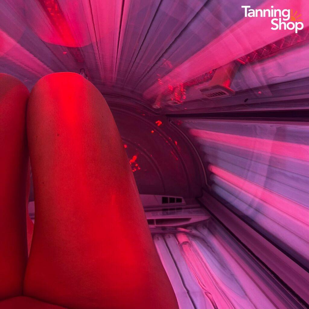 Inside view of a Tanning Shop red light therapy tanning bed session, showing legs bathed in red and pink LED light for skin rejuvenation and tanning benefits.