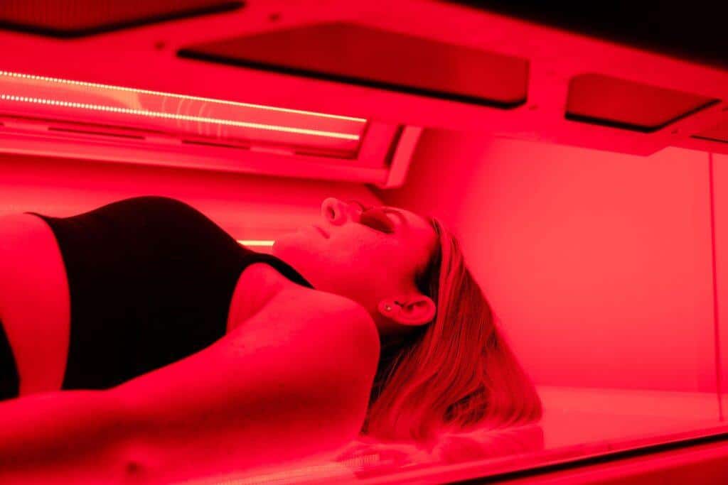 Red Light Therapy The Tanning Shop Woman lying in a red light therapy bed bathed in red LED light at The Tanning Shop