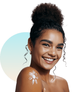 Smiling woman with curly hair in a bun and bare shoulders showing a white sun-shaped tan mark on her shoulder, representing a new UV tanning journey at The Tanning Shop