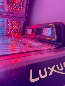 Luxura tanning bed with multi-coloured LED lighting and Luxura branding on the base at The Tanning Shop