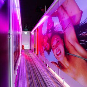 Interior corridor of a Tanning Shop salon with pink neon lighting and a large mural of a smiling woman