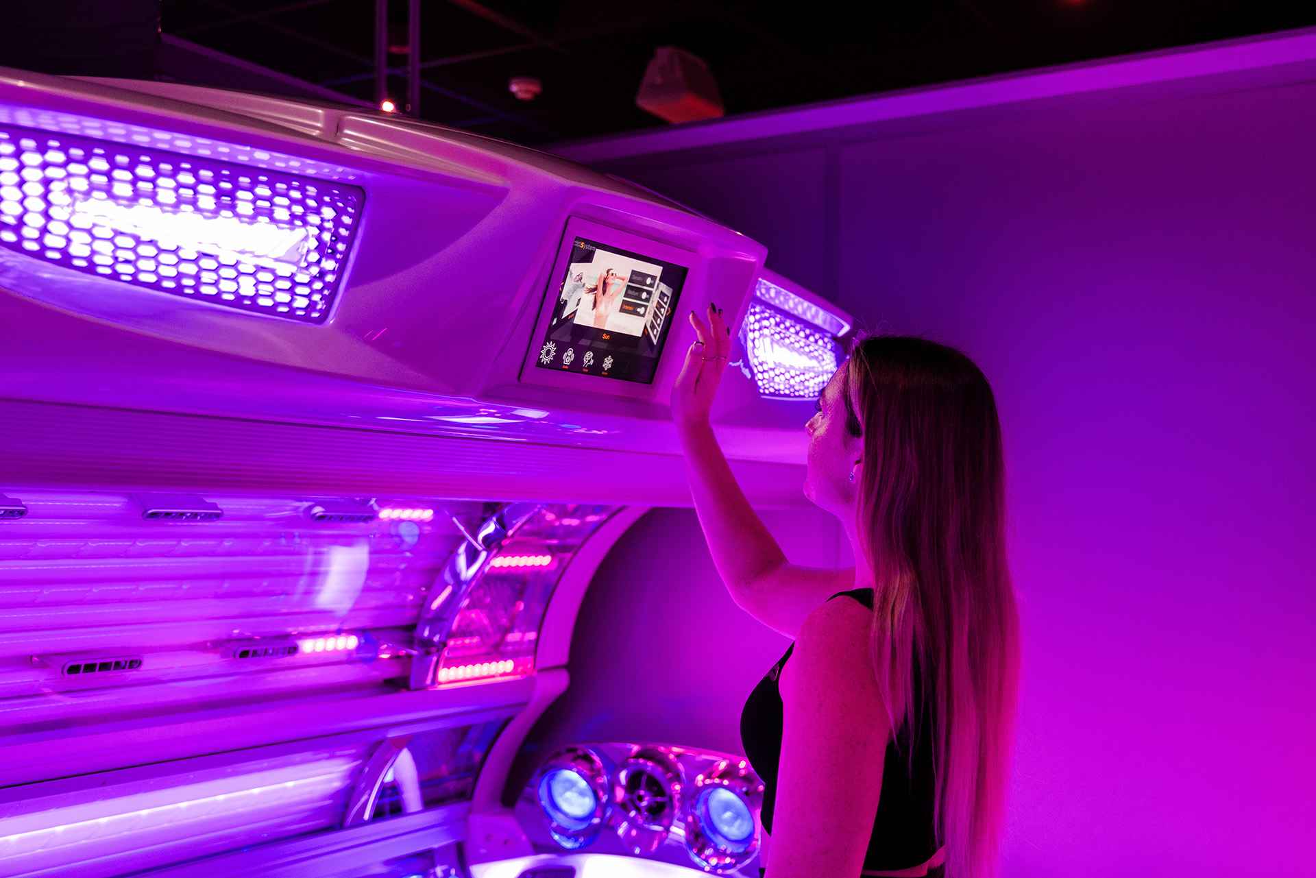 Woman operating the touchscreen control panel on a professional UV sunbed at a Tanning Shop UK salon