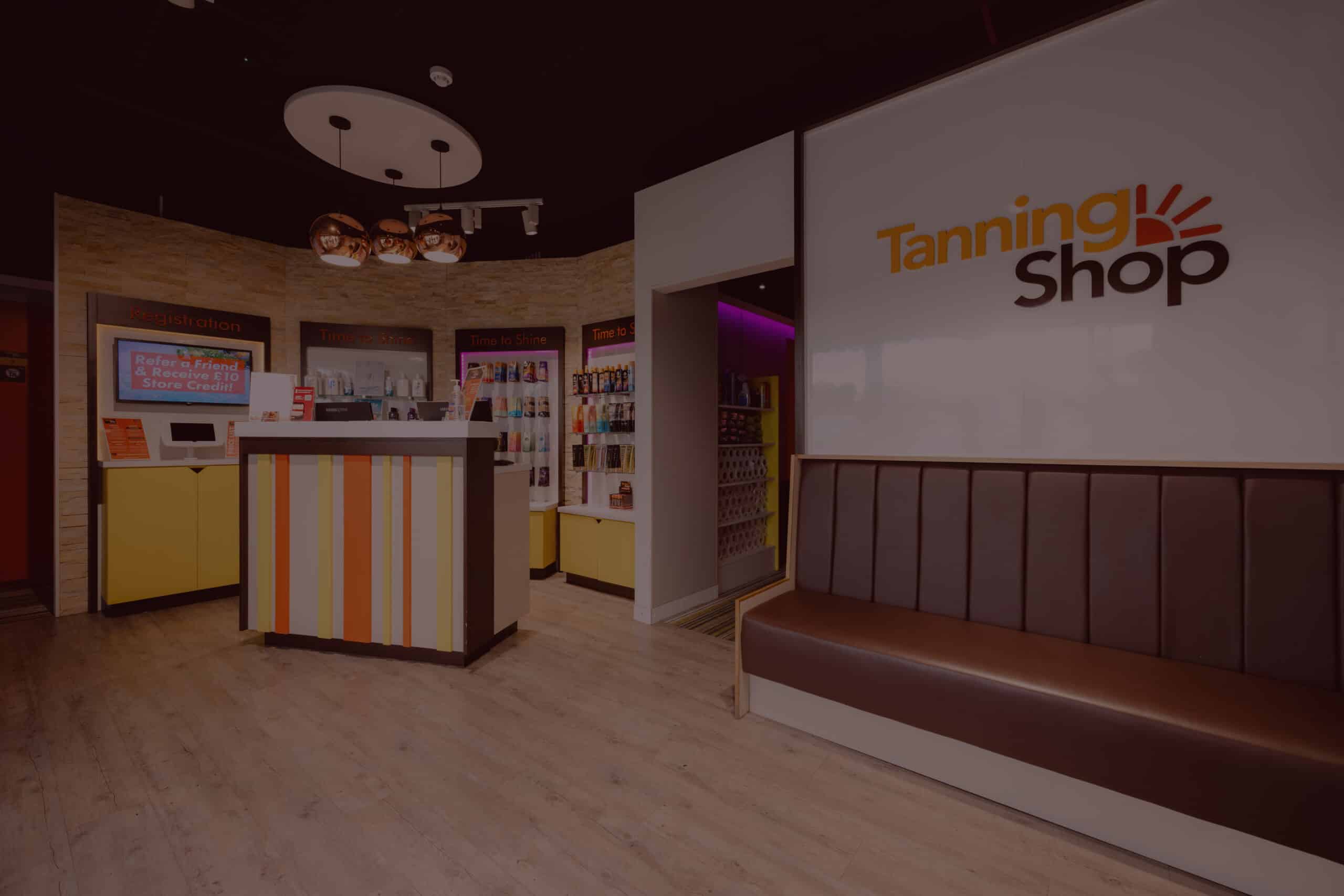 Interior of a Tanning Shop salon showing the reception desk, tanning product displays, and welcoming waiting area at a UK location