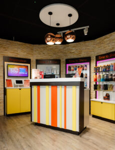 The Tanning Shop salon reception area with registration kiosk, tanning lotion product display, and Time to Shine tanning room entrances