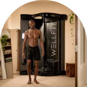 Smiling customer stepping out of a WellFit spray skincare booth after a full-body skin treatment at The Tanning Shop.