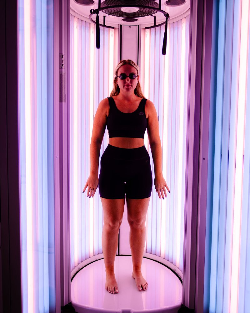 Customer using an advanced stand-up UV tanning booth after a WellFit skincare treatment at The Tanning Shop.