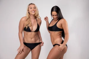 Two smiling women in black swimwear showcasing the natural-looking, bronzed results of a Norvell spray tan at The Tanning Shop. Two smiling women in black swimwear showcasing the natural-looking, bronzed results of a Norvell spray tan at The Tanning Shop.